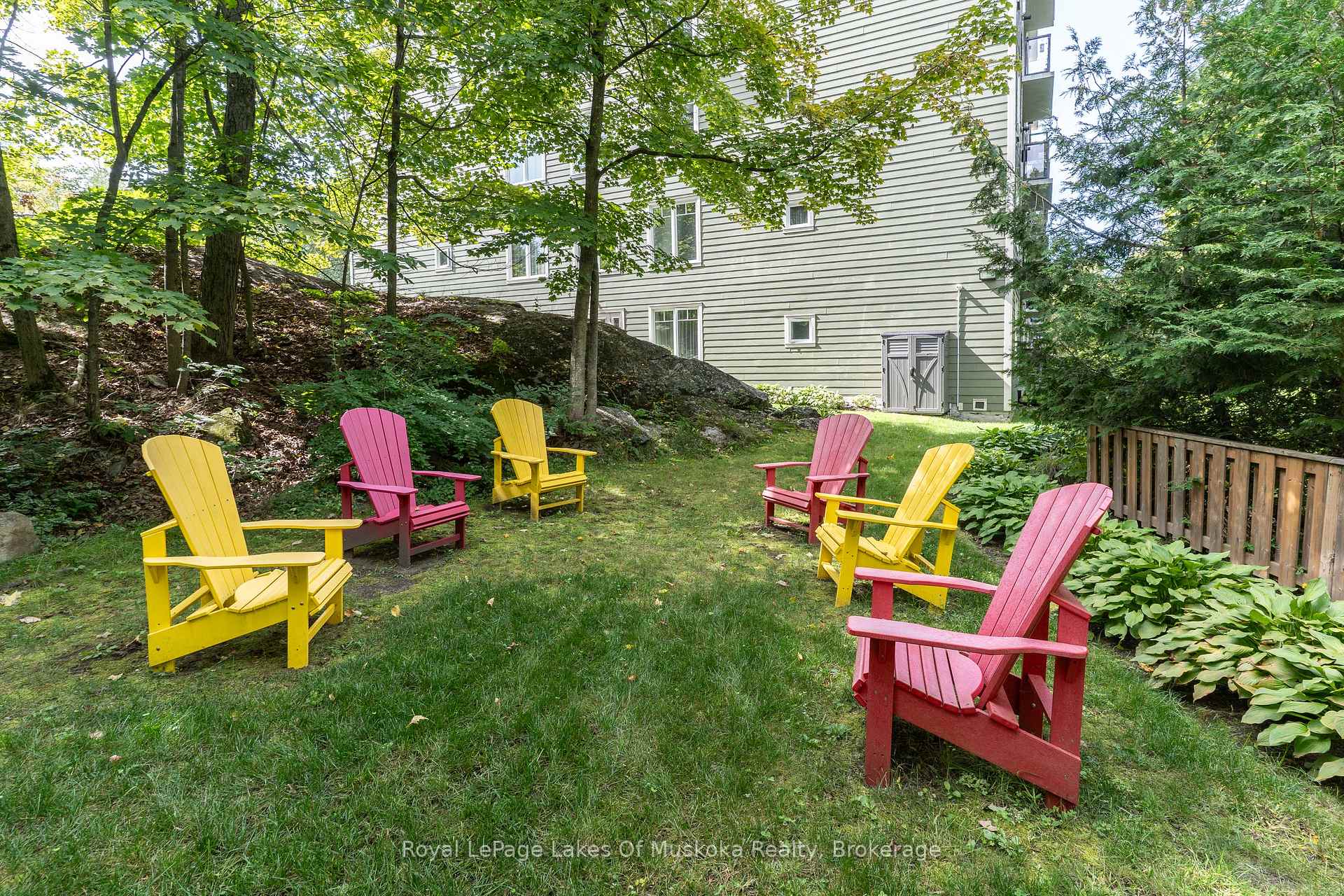 Shaded courtyard lawn beside a building, furnished with colorful Adirondack chairs.
