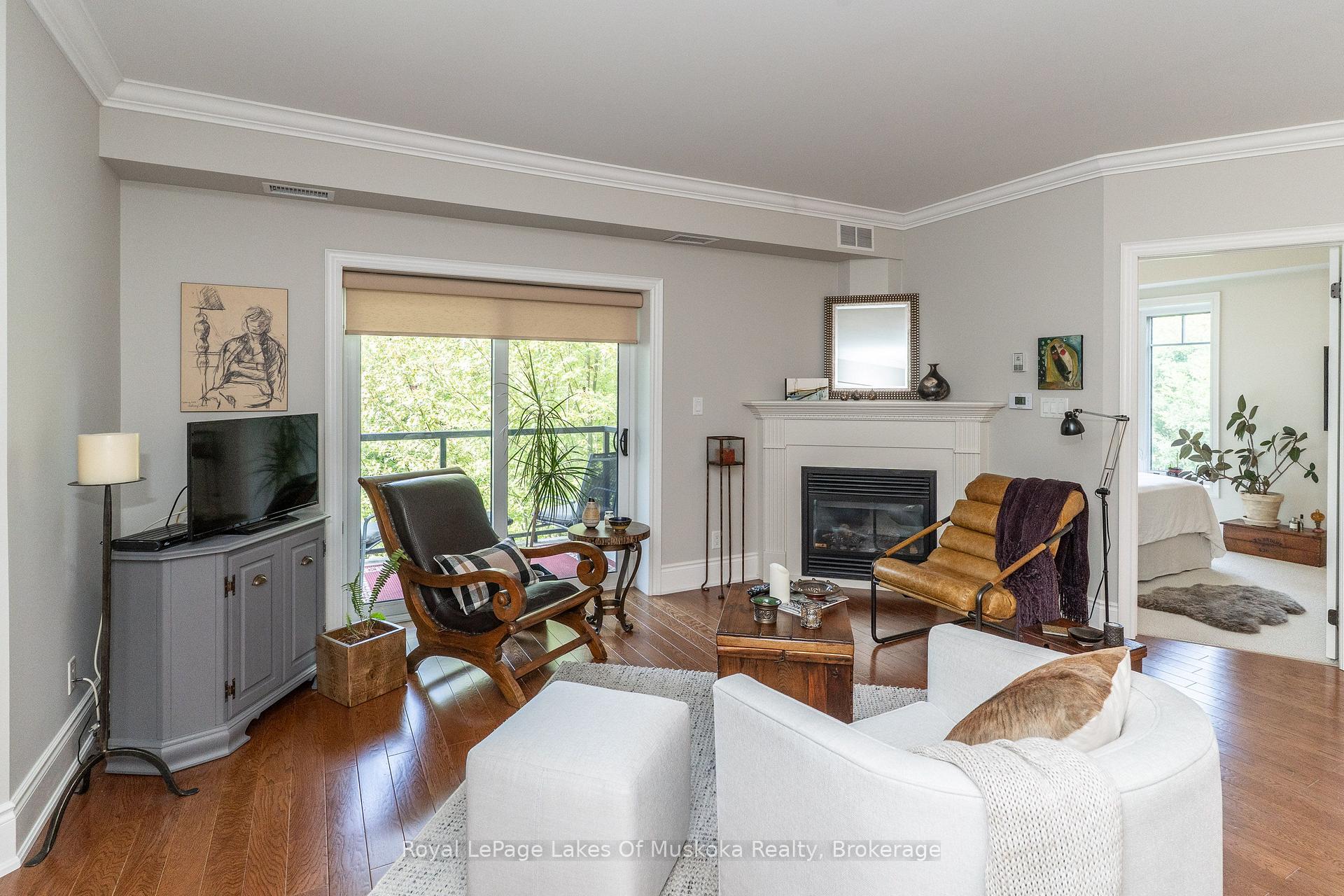 Furnished living room with a white fireplace, hardwood floors, and a sliding door to a leafy balcony.