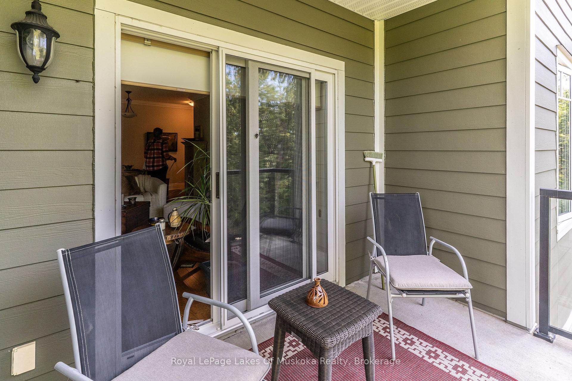 Covered balcony with lounge chairs and a woven table beside sliding glass doors.
