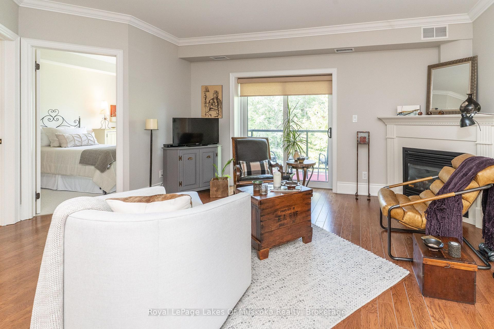 Furnished living room with a fireplace, leather chairs, and sliding doors to a tree-lined balcony.