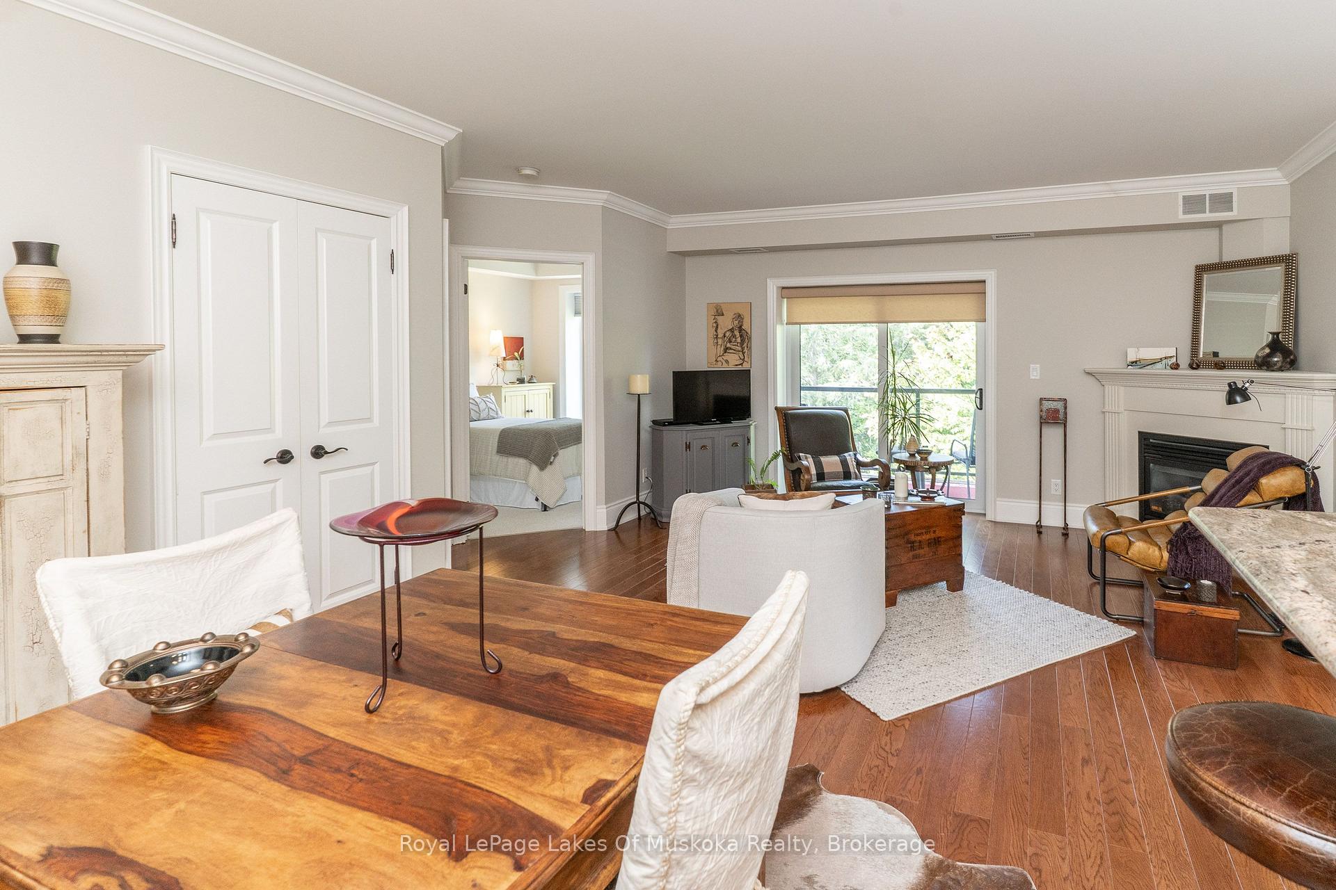 Living and dining area with hardwood floors, fireplace, balcony doors, and an open view into a bedroom.