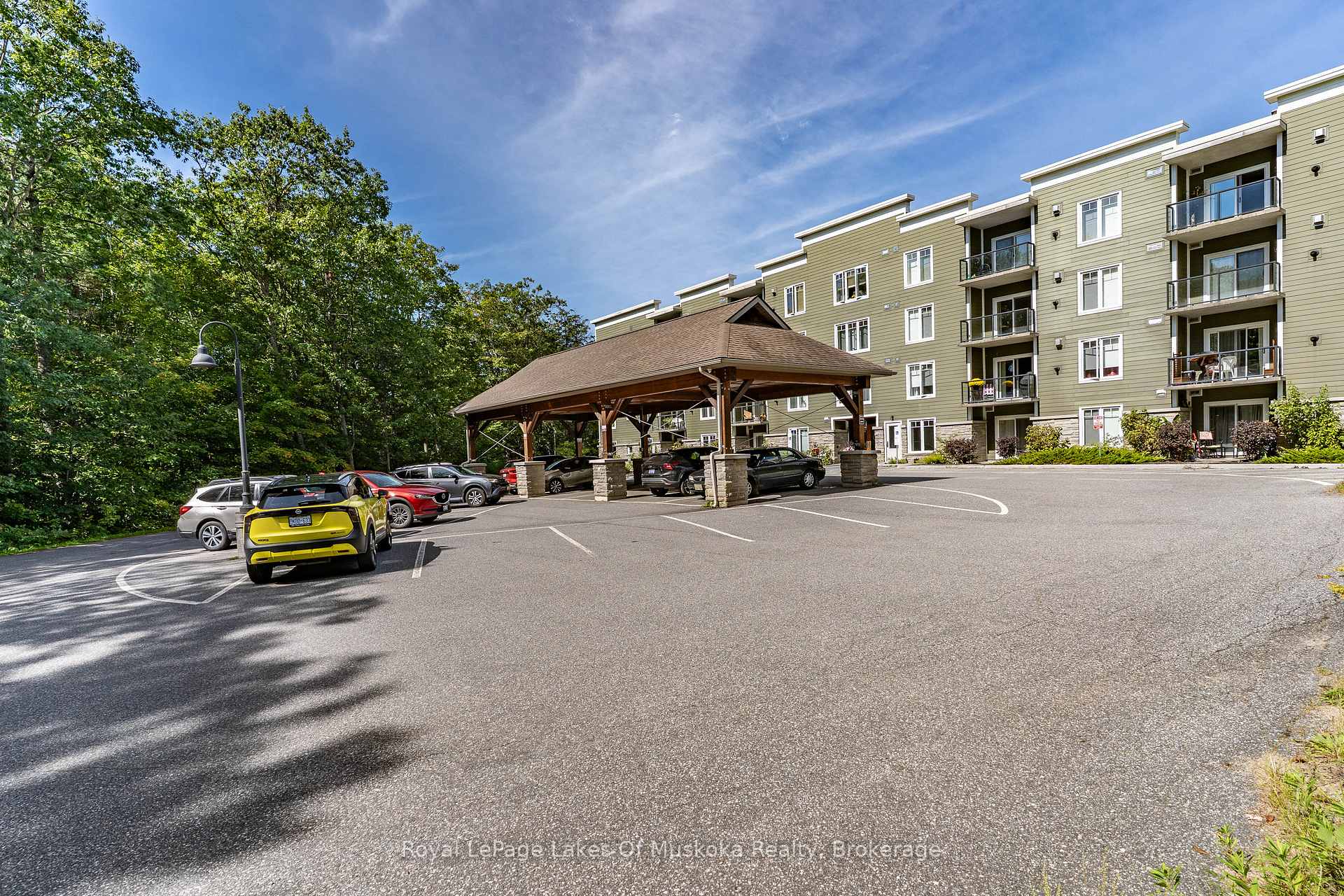 Apartment building exterior with balconies, covered entrance, and parking lot.