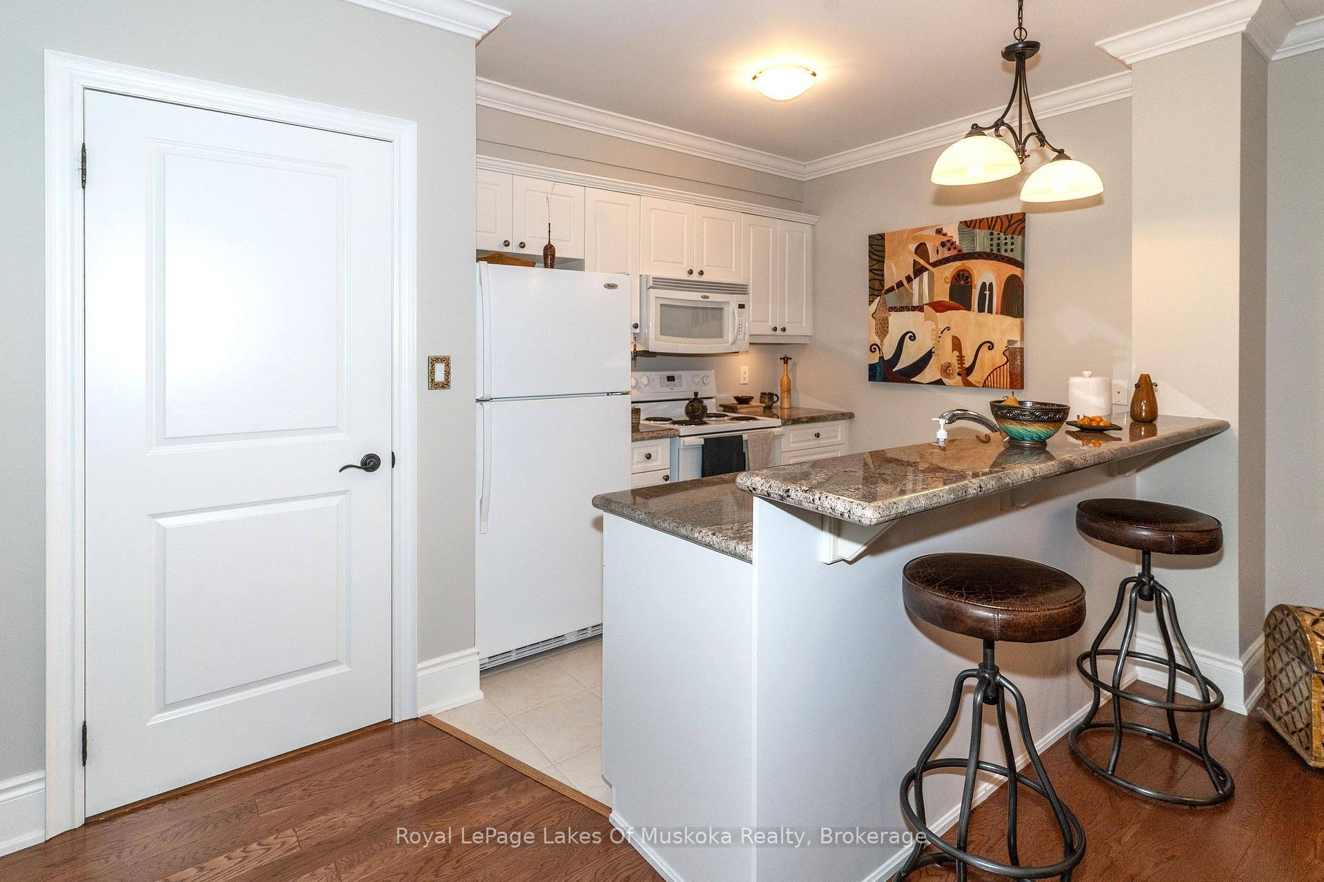 Kitchen with white cabinetry, granite breakfast bar, and two leather stools.