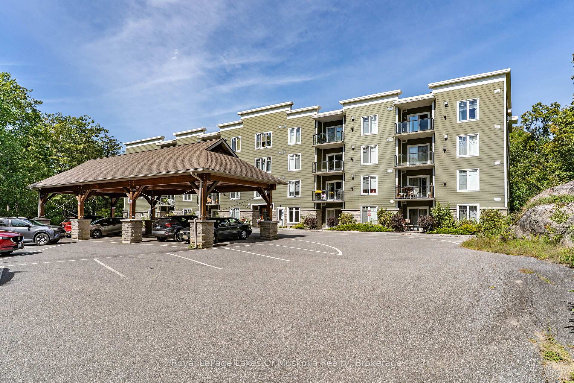 Apartment building with olive-green siding, multiple balconies, and a covered parking canopy.