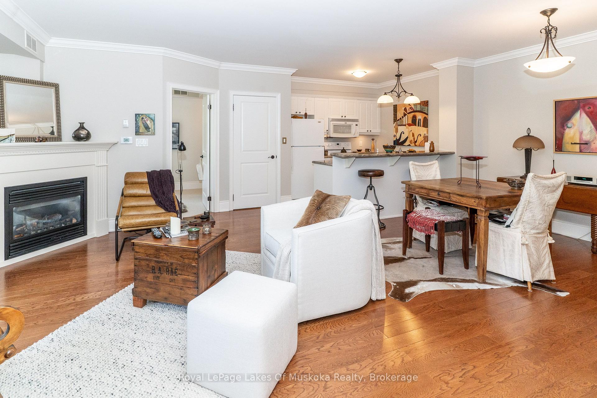 Open-concept condo living and dining room with a gas fireplace, kitchen peninsula, and hardwood floors.