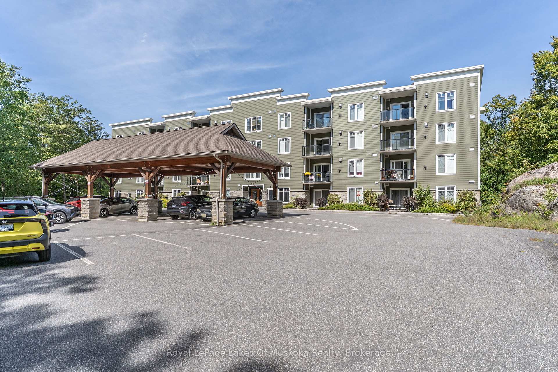Multi-storey green apartment building with balconies and a covered parking area.