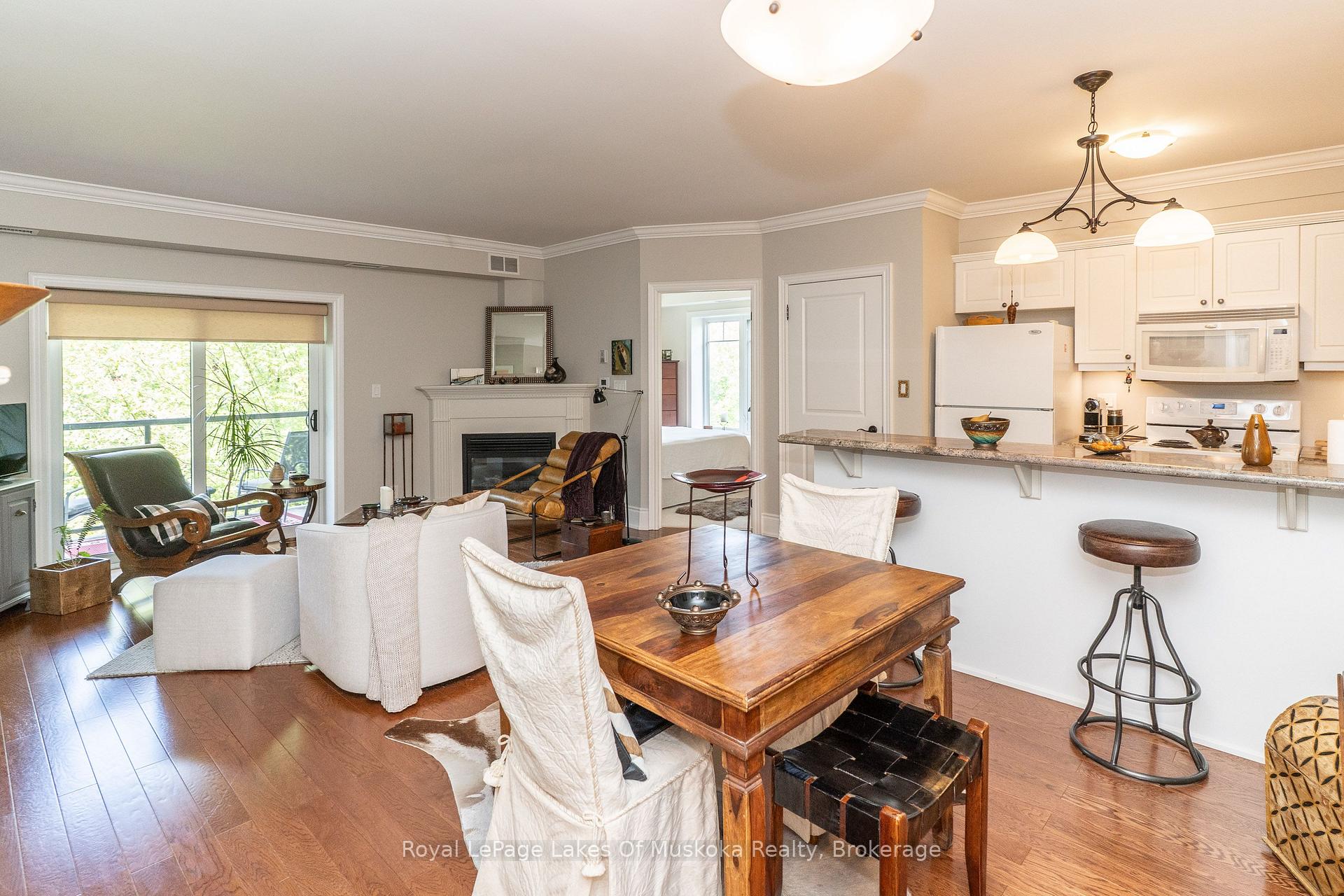 Open-concept living and dining area with a fireplace, hardwood floors, and an adjoining white kitchen.