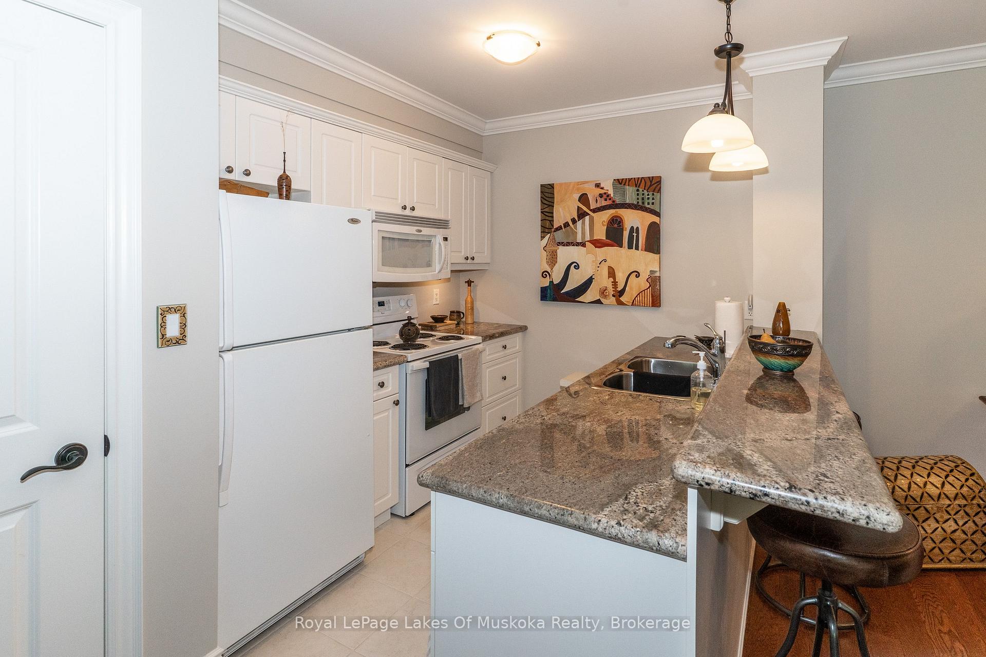 Condo kitchen with white cabinetry, granite counters, and a breakfast bar with stools.