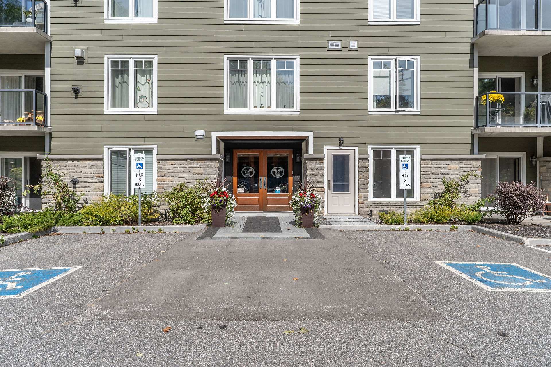 Condominium entrance with stone cladding, wooden double doors, flower planters and accessible parking spaces.