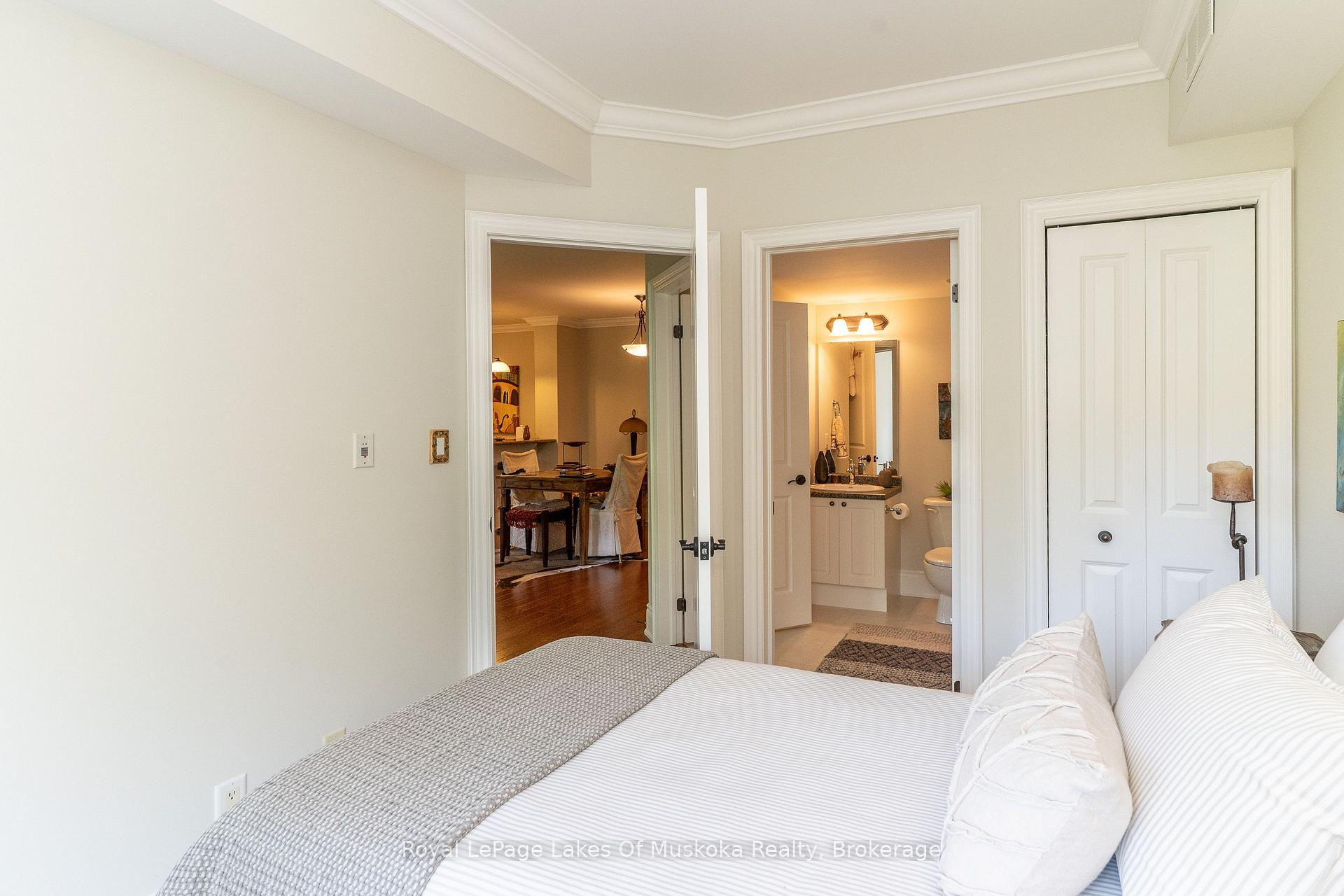 Bedroom with a white bed, tray ceiling, and open doorways to an ensuite bathroom and dining area.