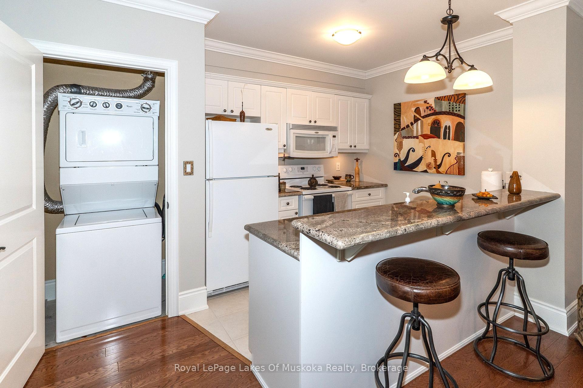 Kitchen with granite breakfast bar and leather stools, white cabinetry, and stacked washer and dryer.