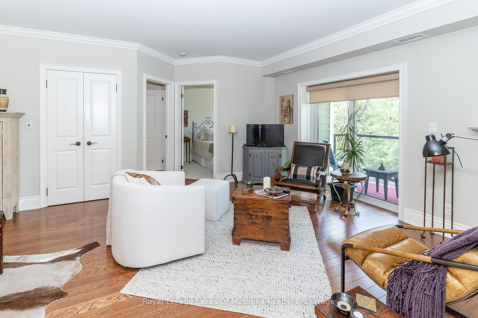 Furnished living room with white seating, hardwood floors, and a large window overlooking leafy trees.