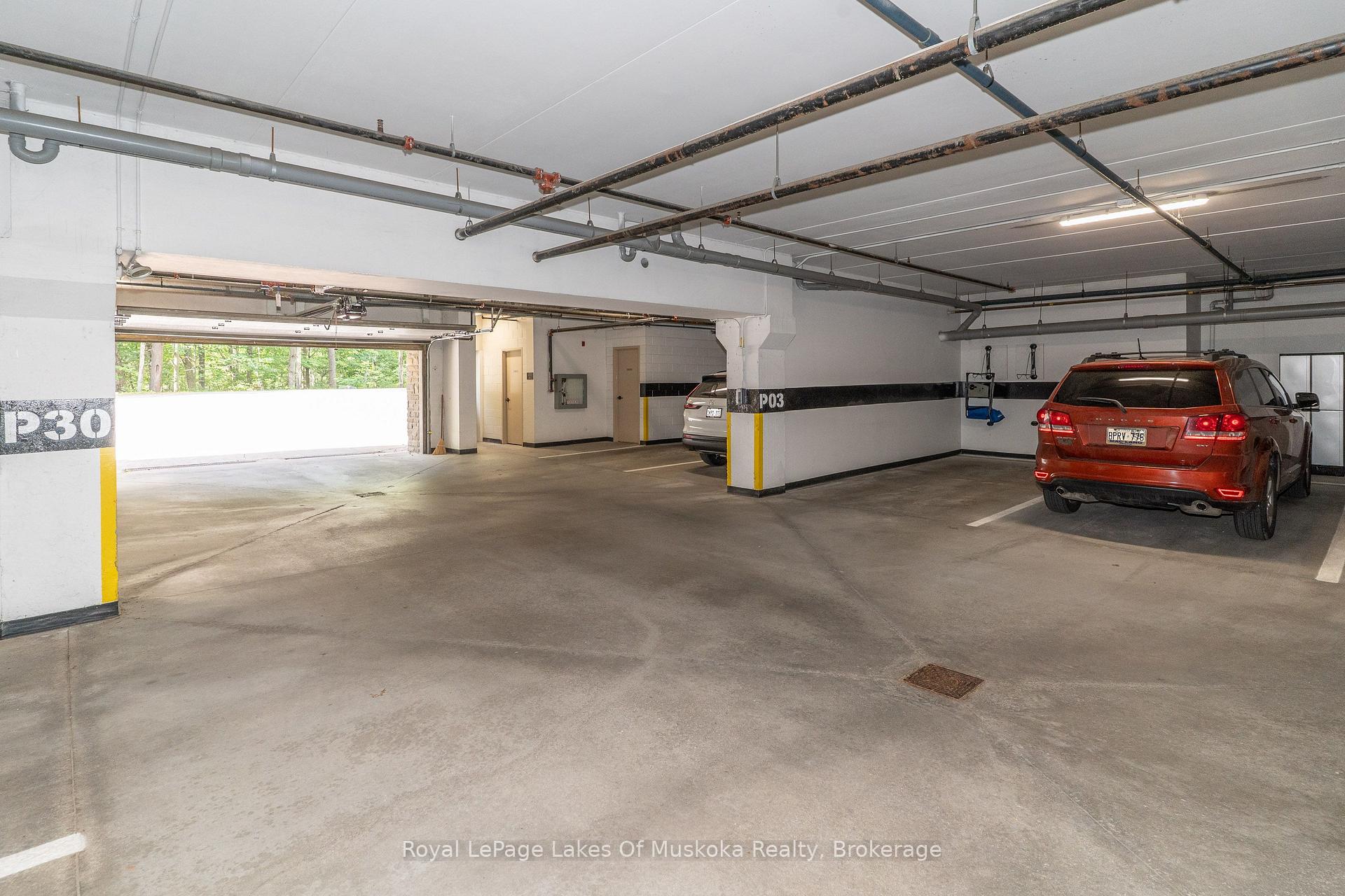Condominium parking garage with numbered columns, exposed pipes, and two parked vehicles.