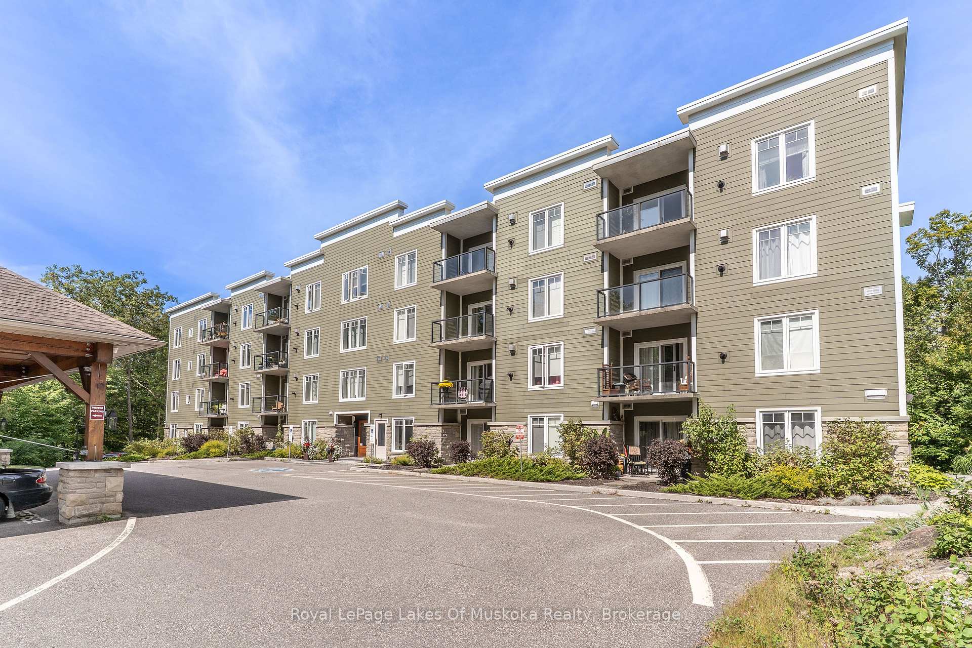 Apartment building with olive-green siding, glass-railed balconies, and a paved parking area.