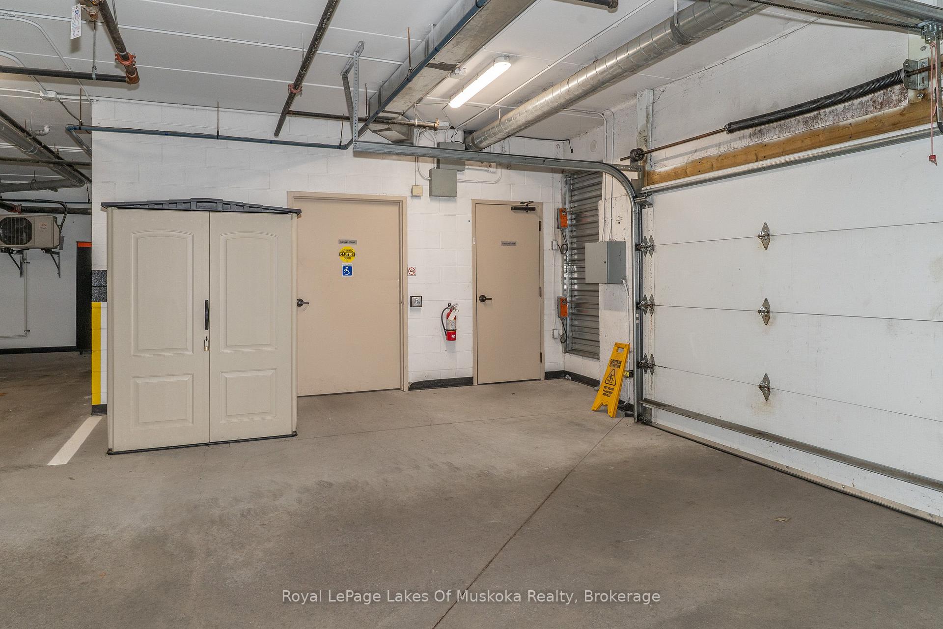 Condominium parking garage with a large overhead door and exposed ceiling pipes.