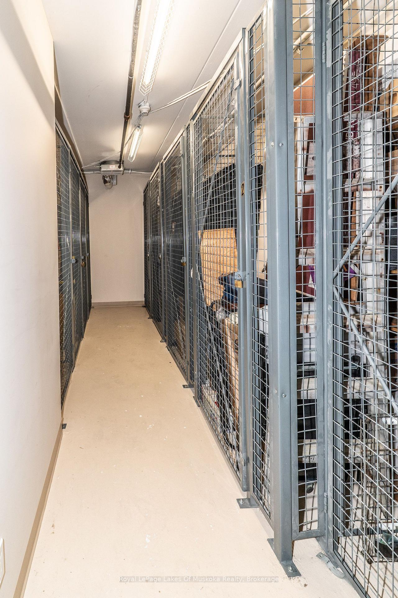 Storage corridor lined with tall gray wire-mesh lockers and lit by overhead fluorescent lights.