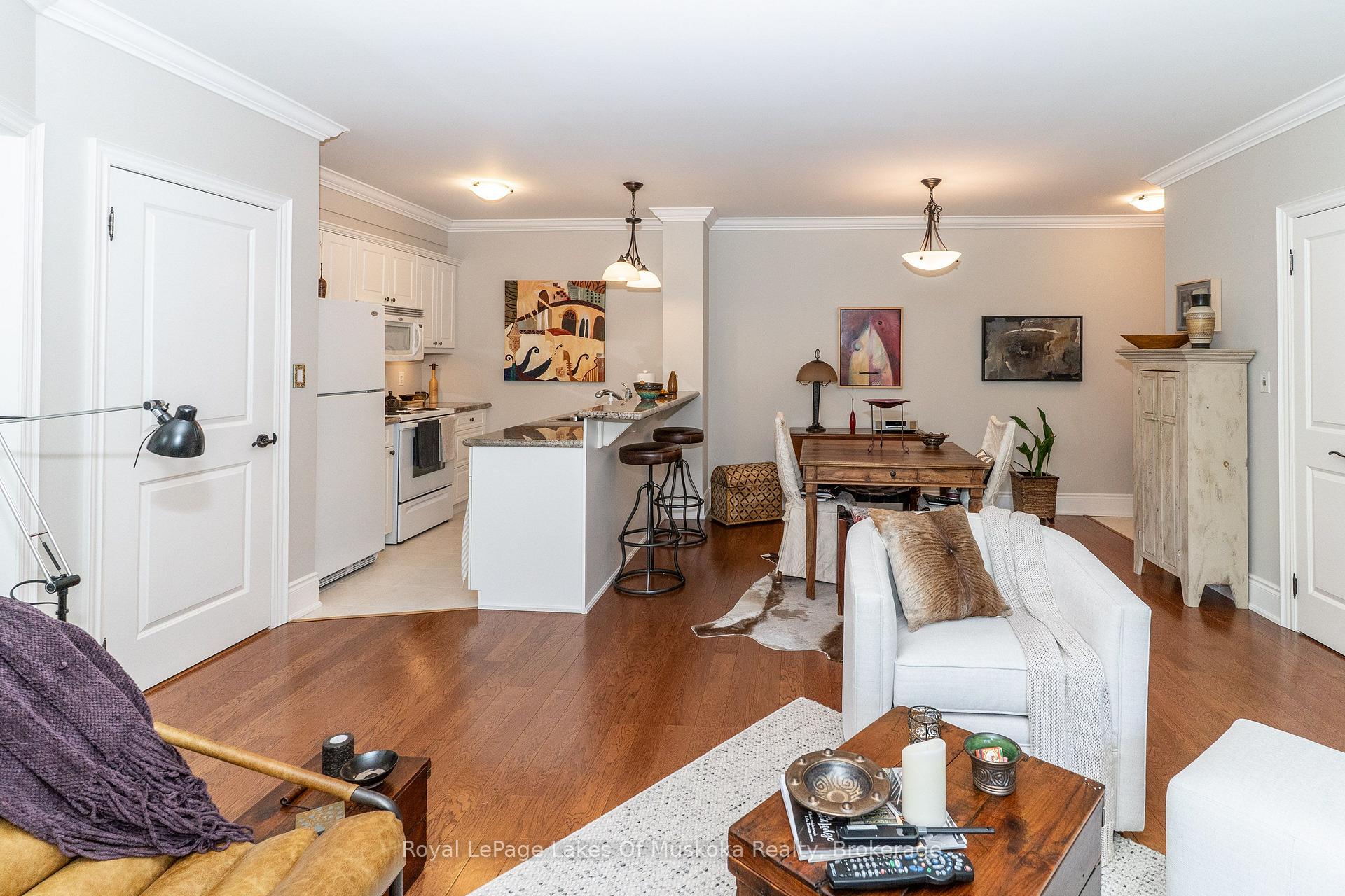 Open-plan living room and kitchen with a breakfast bar, hardwood floors, and a furnished dining area.