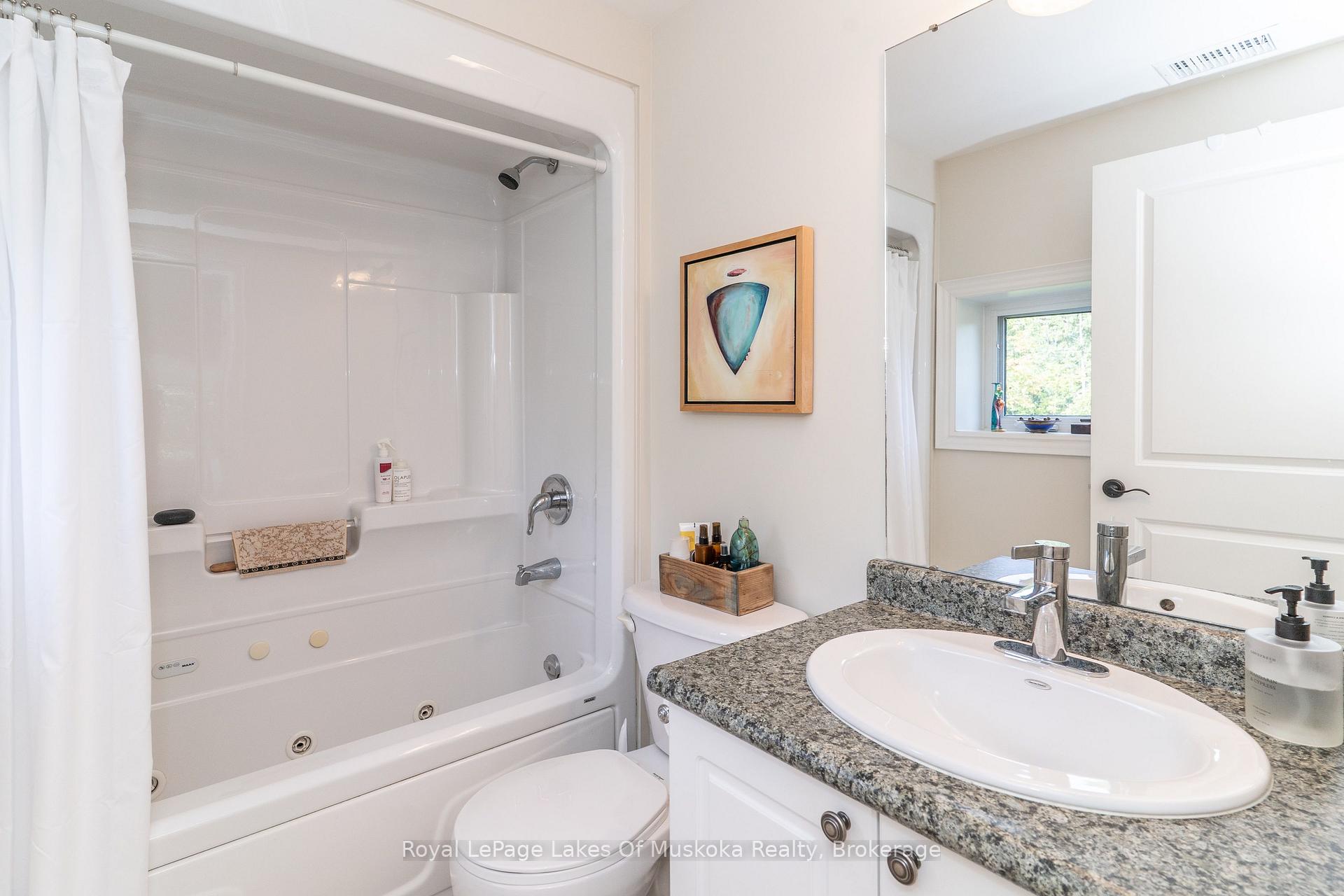 Bathroom with a white tub and shower beside a granite-topped vanity and oval sink.