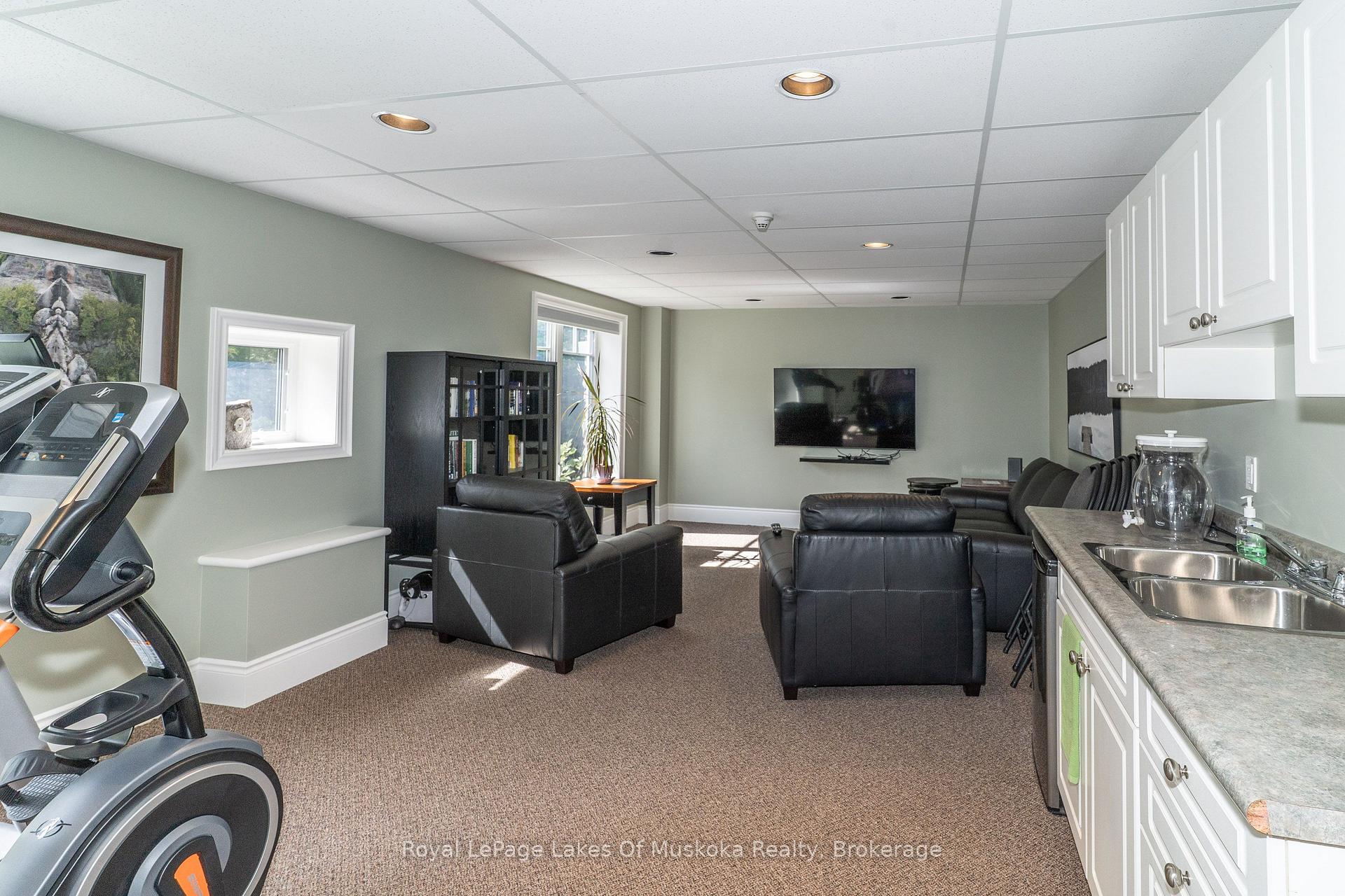 Furnished recreation room with black leather sofas, exercise equipment, and a kitchenette.