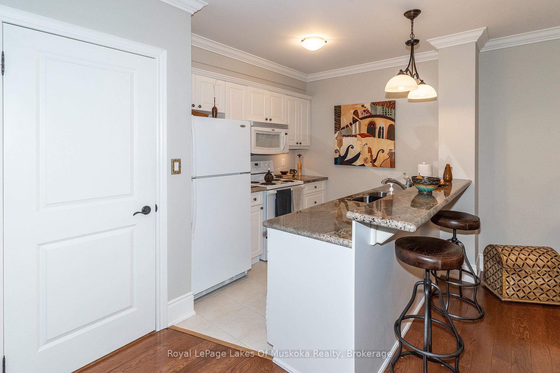Kitchen with white cabinetry, granite breakfast bar, and two dark leather stools.