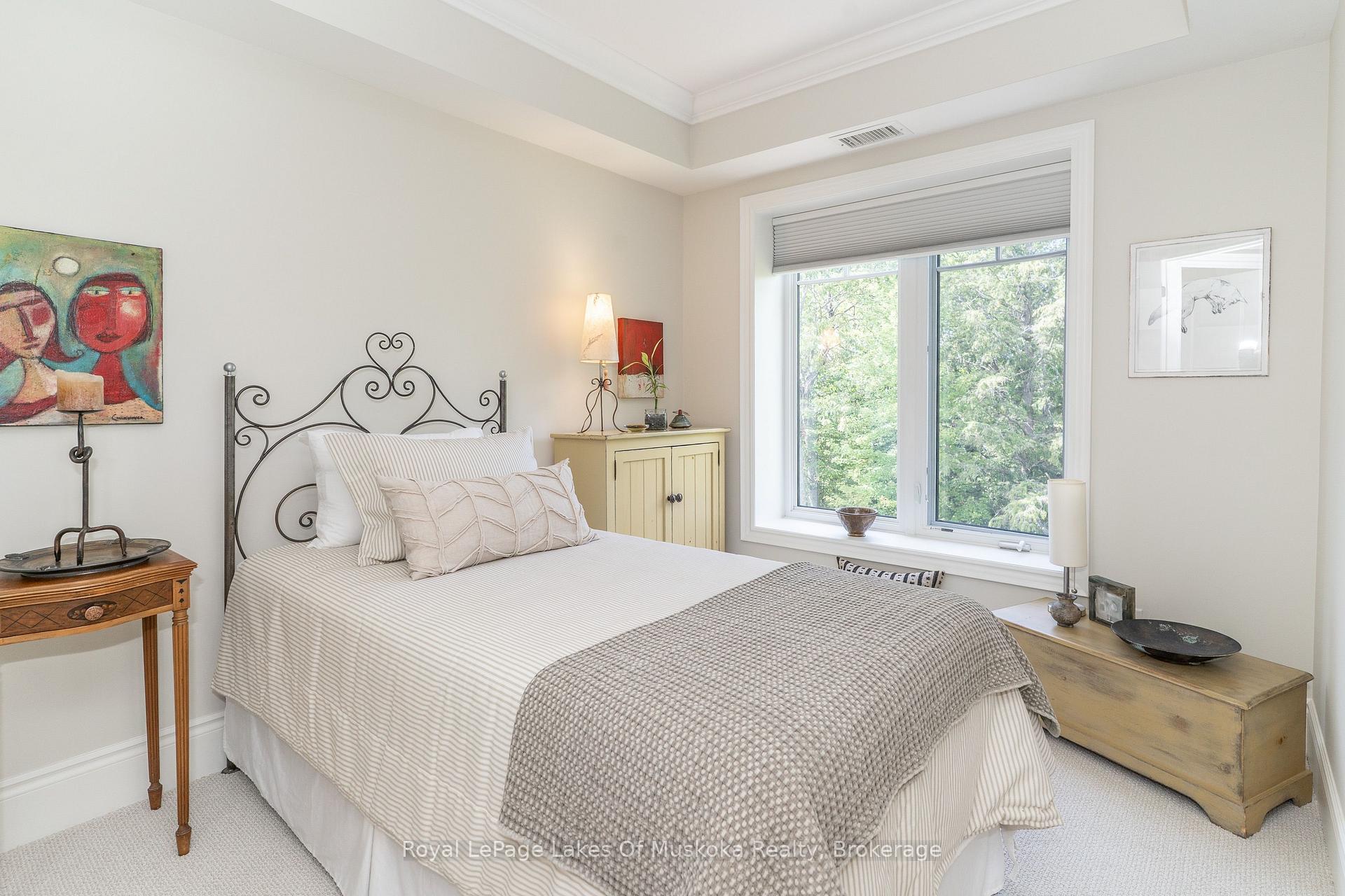Staged bedroom with an ornate metal bed and large window overlooking trees.