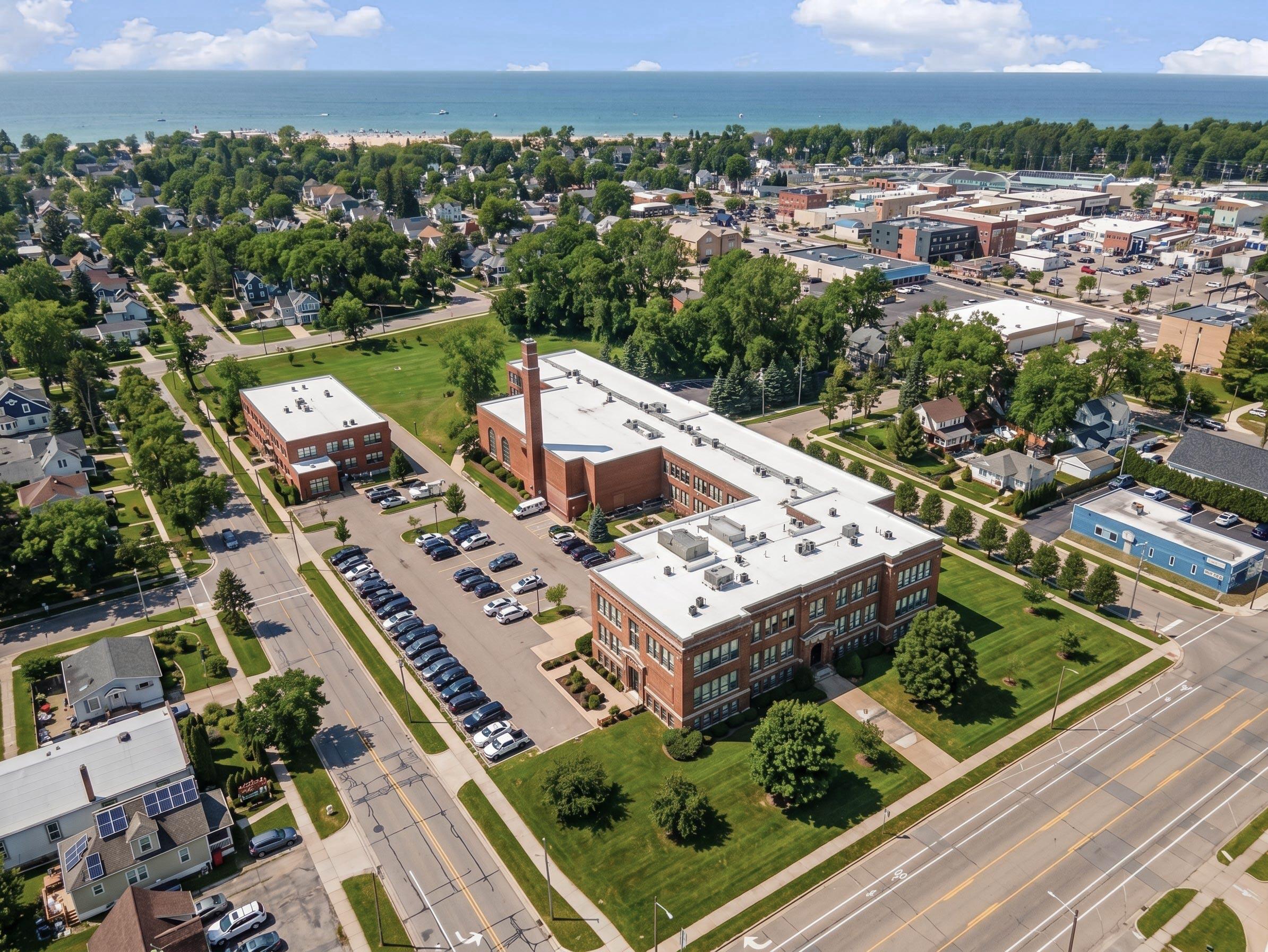 Aerial view of a lakeside town, with a large brick building in the foreground and the beach and lake beyond.