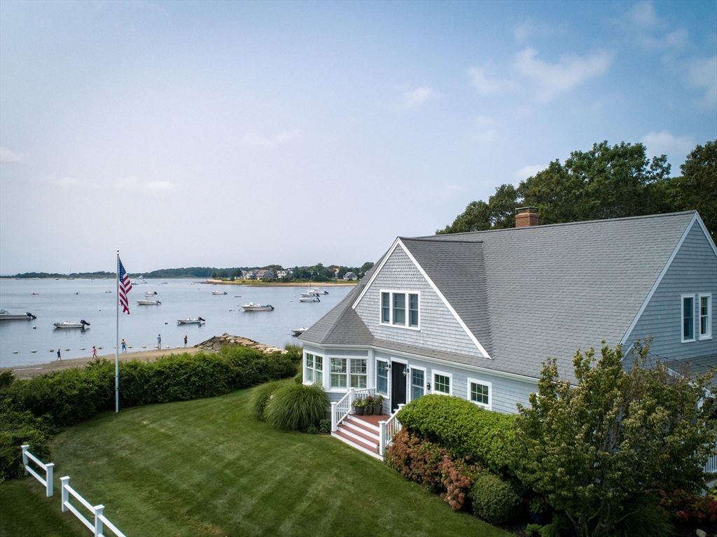 Waterfront shingled home with a manicured lawn overlooking a bay dotted with boats.