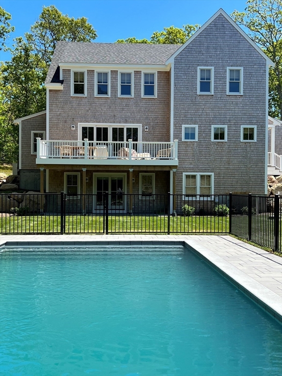 Gray shingle-sided house behind a swimming pool, with a white-railed deck and black fence.
