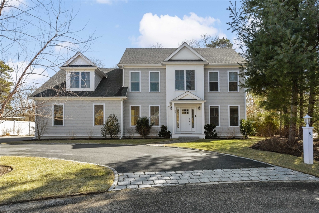 Two-story gray shingle house with white trim, central entry, and curved stone walkway.