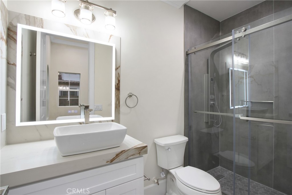Modern bathroom with a vessel sink, illuminated mirror, and glass-enclosed gray-tile shower.