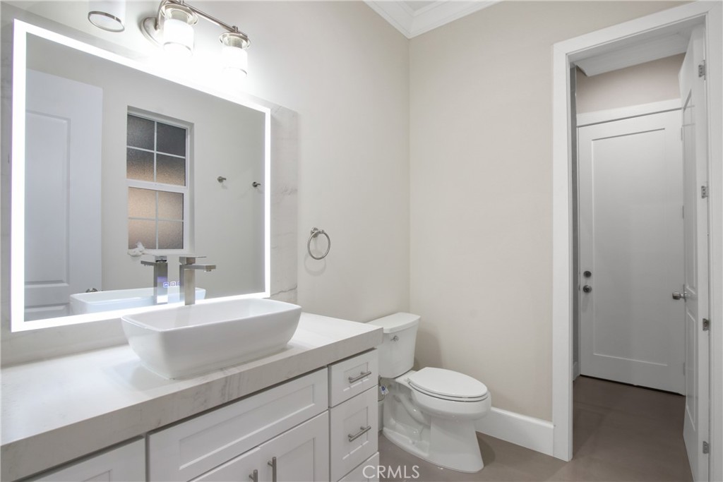 Bathroom with a white vessel sink, illuminated mirror, and toilet beside an open doorway.