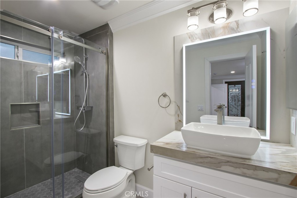 Bathroom with a glass-enclosed dark-tile shower and a white vessel sink on a marble-look vanity.