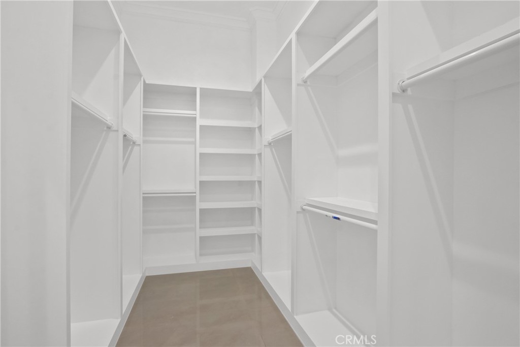 Walk-in closet with white built-in shelving and hanging rods, and a brown tile floor.
