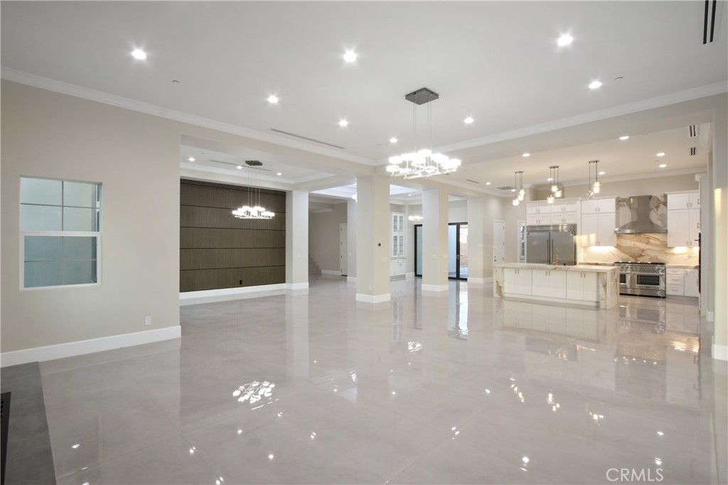 Vacant open-plan living area with glossy tile floors, a white kitchen, and a dark paneled accent wall.