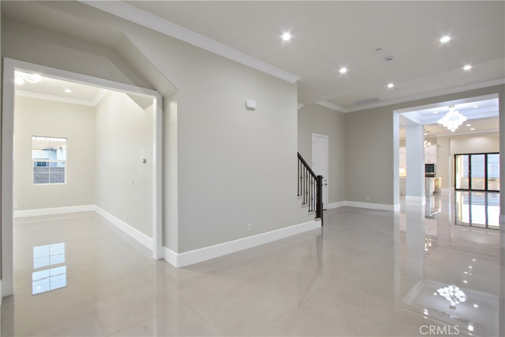 Bright vacant interior with glossy tile floors, an adjoining room, and a staircase.