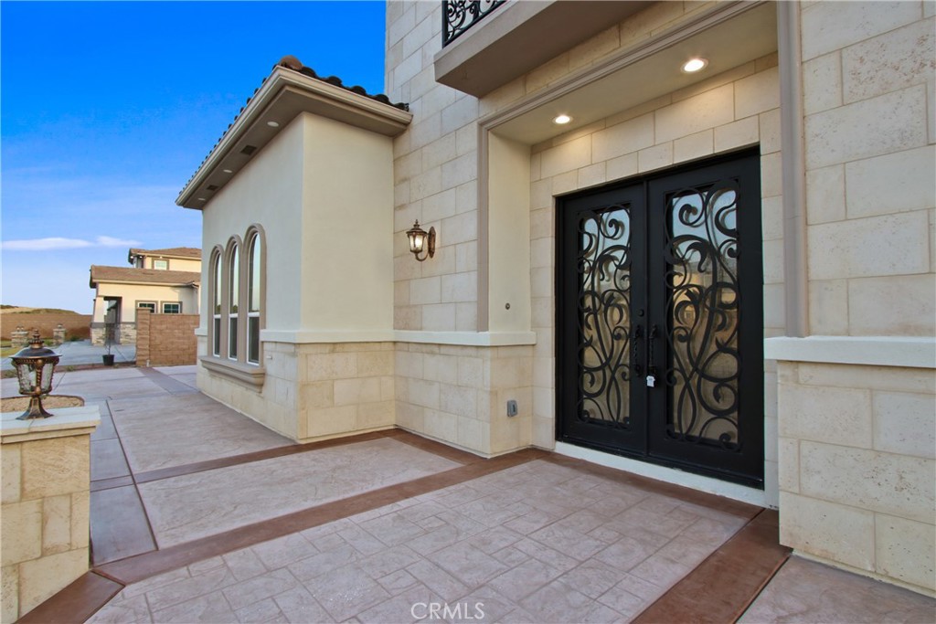 Stone home entrance with ornate black double doors and a broad tiled patio.