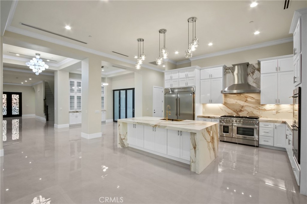 Modern kitchen with a large marble island, white cabinetry, and stainless steel appliances.