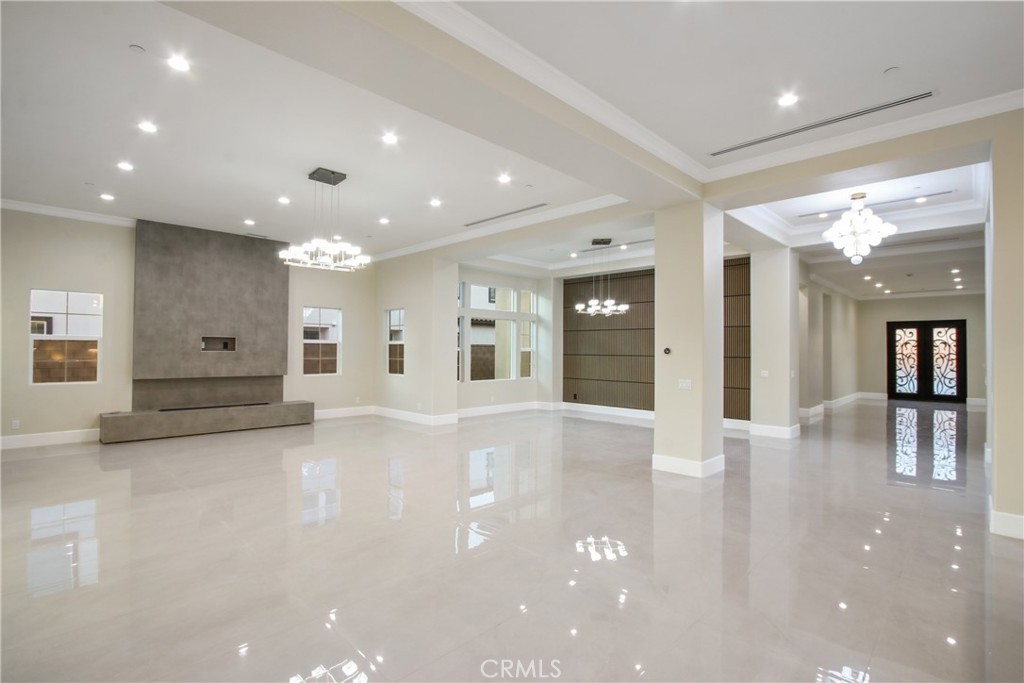 Vacant living area with a gray fireplace feature wall, glossy tile floors, and chandeliers.