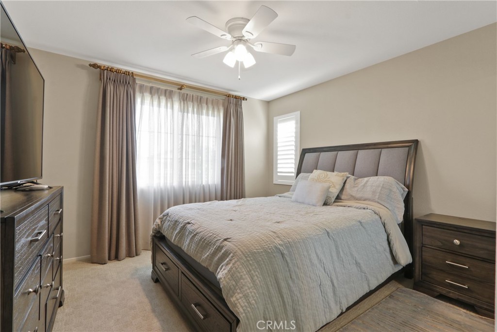 Furnished bedroom with a dark wood bed, gray bedding, ceiling fan, and curtained window.