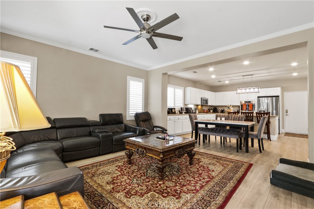 Open-plan living room and kitchen with a leather sectional, ornate rug, and white cabinetry.