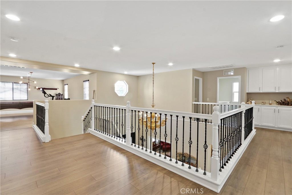 Upstairs landing with black iron stair railings, light wood floors, and a gold chandelier.
