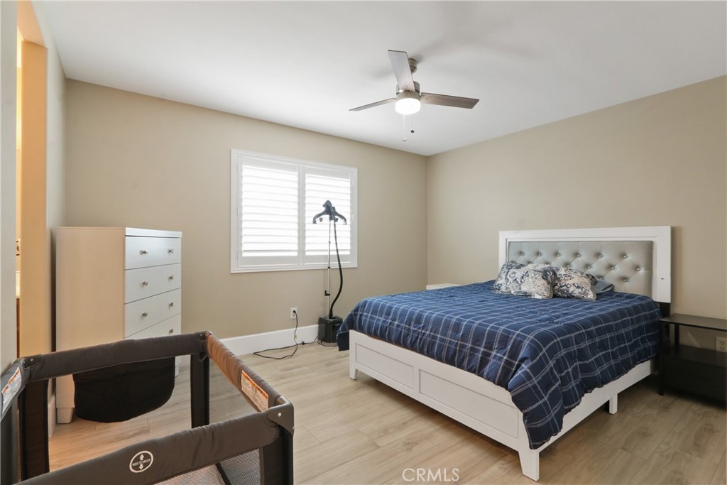 Bedroom with a white bed, blue plaid bedding, shuttered window, and playpen in the foreground.