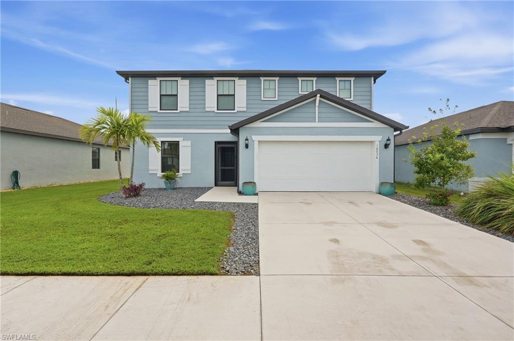 Two-story light blue home with a double garage, broad driveway, and small palm tree in the front yard.