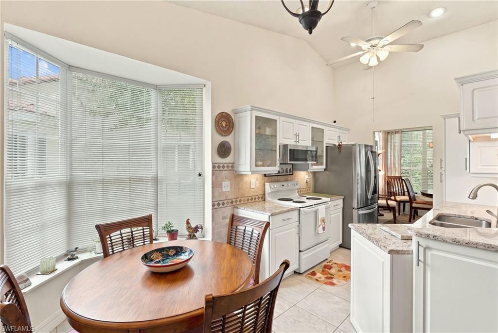 Kitchen and dining area with white cabinets, stainless appliances, and a round table by a bay window.