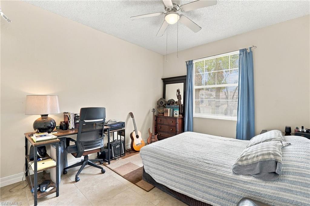 Bedroom with a large bed, desk, guitars, and blue curtains beside a bright window.