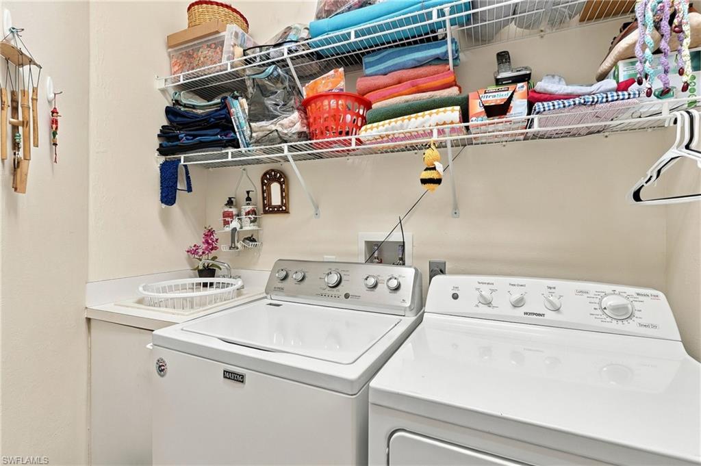 Laundry room with a top-loading washer, dryer, utility sink, and storage shelves above.