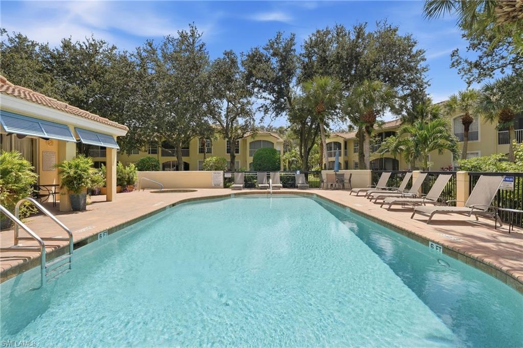 Community swimming pool with lounge chairs, palm trees, and yellow residential buildings.