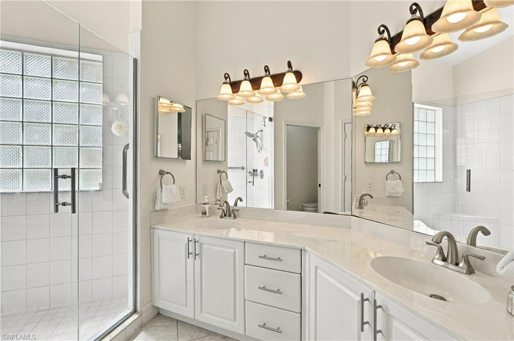 Bathroom with a long double vanity and tiled shower beside glass-block windows.