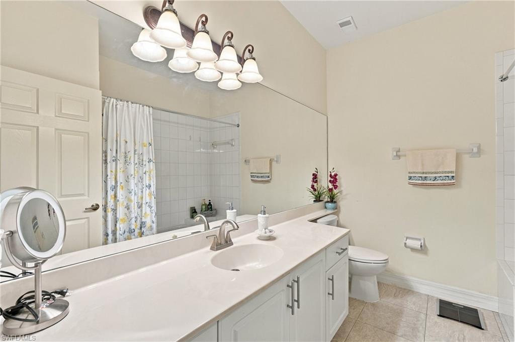 Bathroom with a long white vanity, large mirror, floral shower curtain, and toilet.