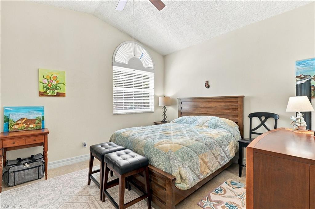 Bedroom with a wooden bed, blue-green quilt, arched window, and black upholstered stools.